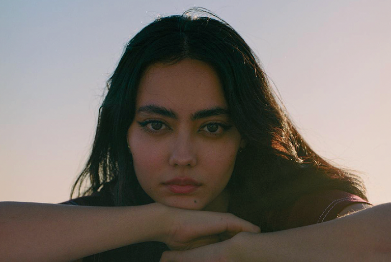 Close-up portrait of musician Tamara Montina resting her chin on her crossed arms outdoors in warm sunlight.